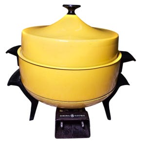 May include: A bright yellow electric skillet with a matching domed lid and black handles. The base features a black control housing with the text General Electric printed in white. The appliance stands on four black legs and includes a power port.