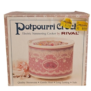 Peut inclure: Une boîte en carton carrée pour un mijoteur électrique Rival Potpourri Crock. La boîte présente un motif de dentelle rose et blanc, un graphique de rose et du texte incluant Potpourri Crock, Electric Simmering Cooker et Quality Stoneware.
