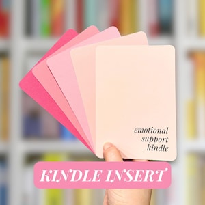 May include: A set of five pink paper inserts for a Kindle e-reader. The inserts are arranged in a fan shape, with the largest insert at the bottom. The largest insert has the text "emotional support kindle" printed on it. The text "KINDLE INSERT" is printed in pink on a white background at the bottom of the image.