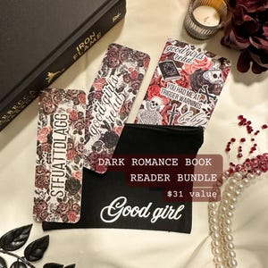 May include: A dark romance book reader bundle featuring floral bookmarks and a black pouch with the words "Good girl". The bookmarks have floral and skull designs. The book "Iron Flame" is also visible.