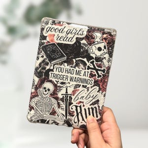 May include: A clear protective case for an e-reader, decorated with stickers. The stickers include a skull, roses, a book, and the phrases "good girls read" and "You had me at trigger warnings".