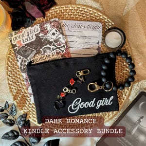 May include: A dark romance Kindle accessory bundle featuring a black zippered pouch with "Good girl" text, a beaded bracelet, a decorative bookmark, and a small candle. The bundle includes decorative charms and a book-themed bookmark.