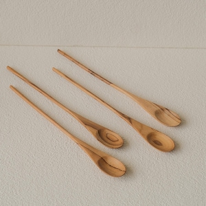 Op de afbeelding: Vier houten lepels met lange, slanke handvatten en ovaalvormige kommen zijn diagonaal gerangschikt. De lepels zijn lichtbruin van kleur met zichtbare houtnerf. De lepels lijken gemaakt te zijn van een natuurlijk houtmateriaal.