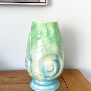 May include: A ceramic vase featuring a glossy finish with a colour gradient transitioning from light green at the top to blue at the base. The surface is decorated with embossed spiral patterns and swirling textures throughout the body.