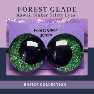 May include: Two 30mm black and green glitter safety eyes from the Basics Collection. The eyes have a black center with a reflective surface and are surrounded by green glitter. The text "FOREST GLADE" and "Kawaii Sinker Safety Eyes" is at the top.