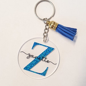 May include: A blue glitter letter Z keychain with a blue tassel and the name "Janette" written in cursive.