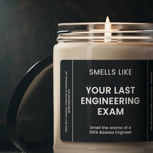 Puede incluir: Una vela de soja beige en un tarro de vidrio con una etiqueta negra que dice "Smells Like Your Last Engineering Exam. Smell the aroma of a 100% Badass Engineer."