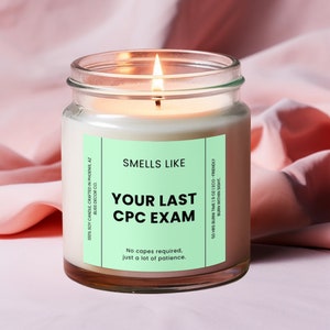 May include: A clear glass candle jar with a white candle inside. The label on the jar is green and says "Smells Like Your Last CPC Exam. No capes required, just a lot of patience."