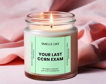 May include: A clear glass candle jar with a white candle inside. The label reads "Smells Like Your Last CCRN Exam" and "No capes required, just a lot of patience."