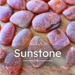 May include: A collection of polished sunstone cabochons in various shapes and sizes, featuring a reddish-orange hue with internal metallic glitter inclusions. The word Sunstone is printed in white text across the centre of the image.