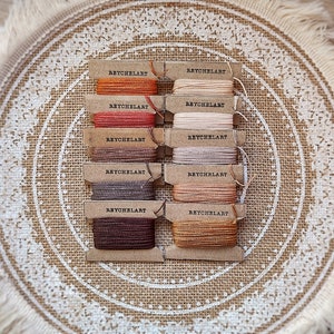 May include: A set of ten spools of embroidery floss in various shades of brown, orange, and beige. Each spool is labeled "REYCHELART".