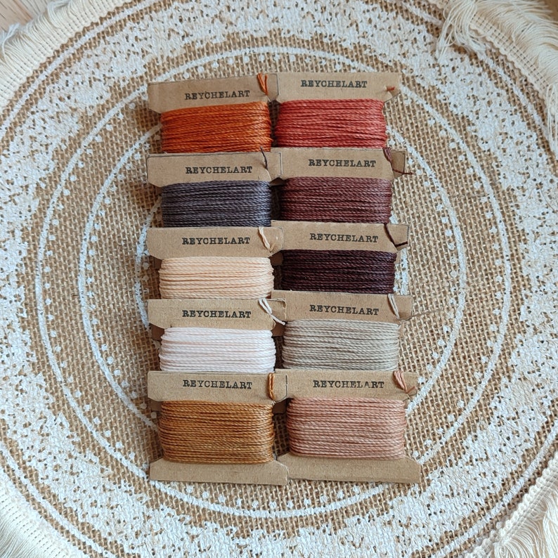 May include: Eight spools of embroidery floss in various shades of brown, beige, and cream. Each spool is labeled "REYCHELART".