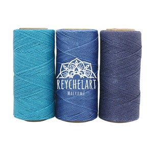 以下が含まれることがあります： 青、ターコイズ、ネイビーの3色のコットンコードの糸巻き。糸巻きには「REYCHELART MACRAME」のラベルが貼られています。