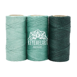 May include: Three spools of macrame cord in shades of green. The spools are arranged side by side, with the middle spool featuring the text "REYCHELART MACRAME" in white. The cord colors range from light teal to deep forest green.