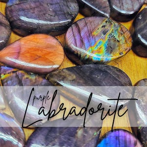Puede incluir: Primer plano de piedras de labradorita pulidas en tonos morados, naranjas y azul iridiscente. Las piedras tienen formas lisas y redondeadas y patrones variados. El texto "purple labradorite" está superpuesto en la imagen.