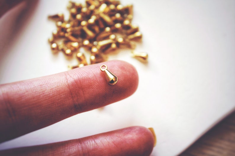 May include: A single gold teardrop-shaped pendant charm with a loop for attaching to a necklace or bracelet.