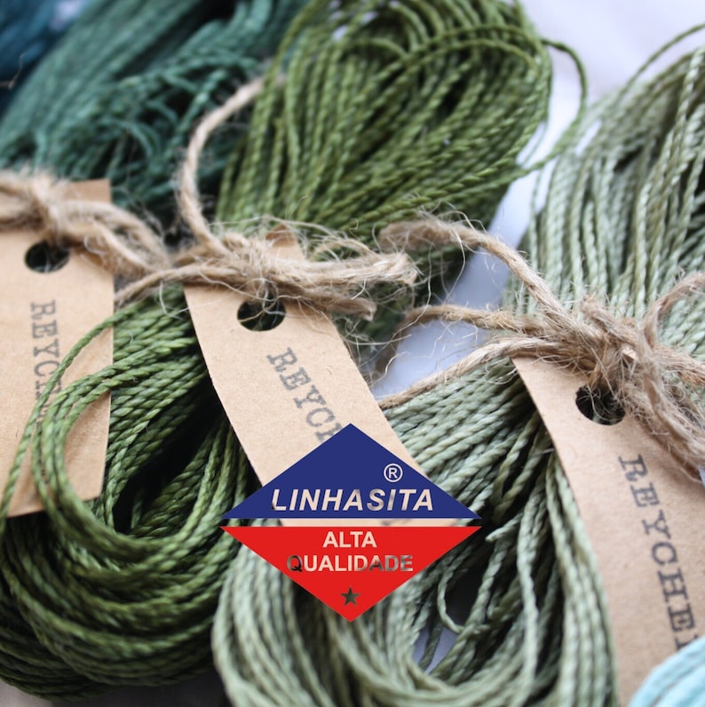 May include: Three spools of green recycled cotton twine with brown paper tags that say "Recycled" and a logo that says "Linhasita Alta Qualidade" with a star.