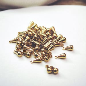 May include: A pile of gold-colored teardrop-shaped metal charms with a small loop at the top.