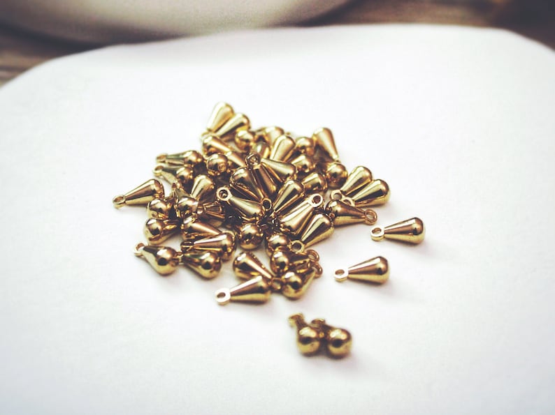 May include: A pile of gold-colored teardrop-shaped metal charms with a small loop at the top.