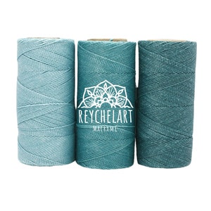 Puede incluir: Tres carretes de cordón de algodón azul turquesa, perfectos para proyectos de macramé. Los carretes están dispuestos uno al lado del otro, con el texto "REYCHELART MACRAME" visible en el carrete del medio.