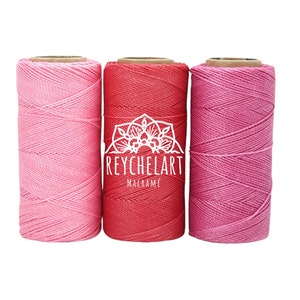 Puede incluir: Tres carretes de cordón de algodón en rosa, rojo y rosa oscuro. Los carretes están etiquetados con "REYCHELART MACRAME".