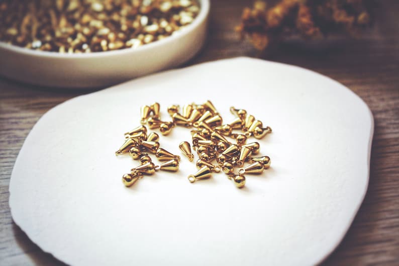 May include: A white plate with a pile of gold-colored teardrop-shaped metal beads.