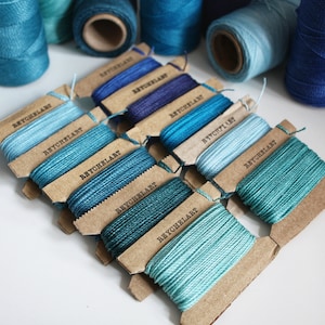 May include: Assortment of blue and teal embroidery floss spools on brown cardboard cards labeled "Beychelar" in black text.