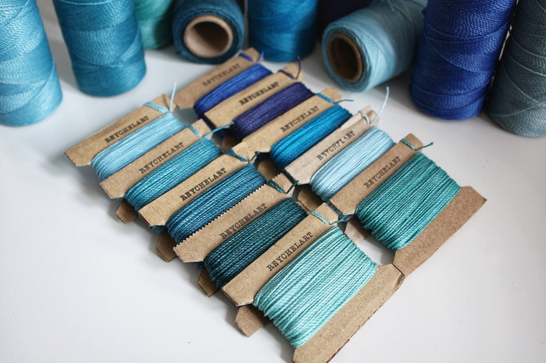 May include: Assortment of blue and teal embroidery floss spools on brown cardboard cards labeled "Beychelar" in black text.