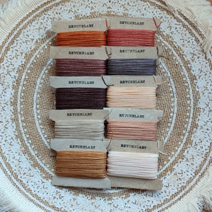 May include: A set of ten spools of embroidery floss in various colors, including brown, beige, orange, and red. Each spool is labeled "REYCHELART".