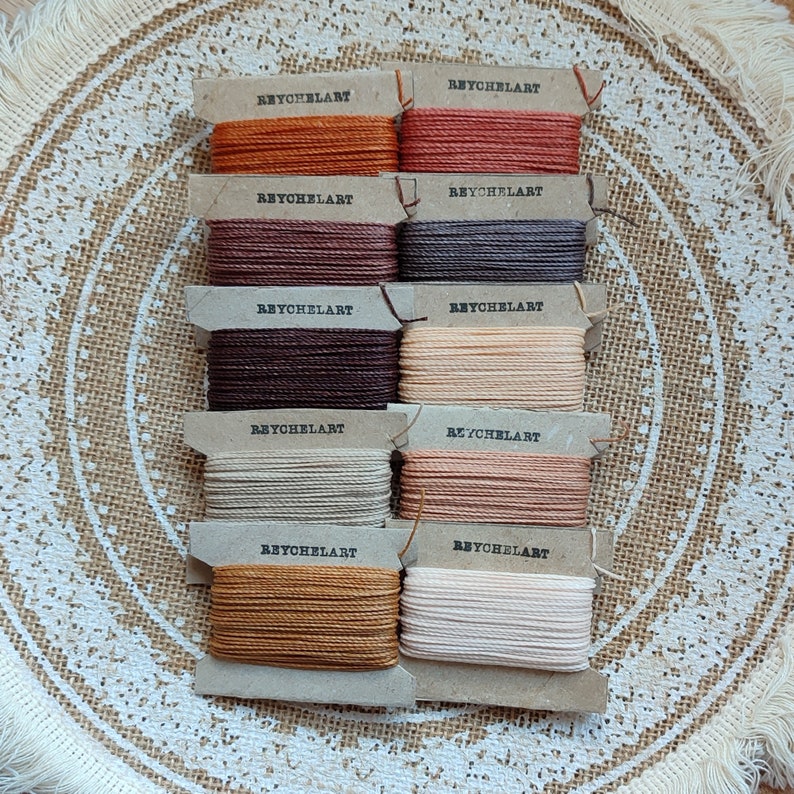 May include: A set of ten spools of embroidery floss in various colors, including brown, beige, orange, and red. Each spool is labeled "REYCHELART".