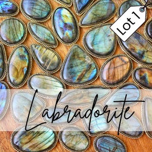 Puede incluir: Una colección de piedras preciosas de labradorita pulidas en varias formas, cada una engastada en un bisel de metal dorado. Las piedras muestran iridiscencias azules, verdes y doradas. La palabra "Labradorita" está superpuesta en la imagen, con una etiqueta "Lote 1".