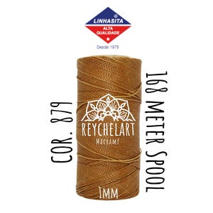 May include: A spool of brown macrame cord with the text "COR. 879", "REYCHELART MACRAME", "1MM", and "168 METER SPOOL". The spool is labeled with the brand "LINHASITA ALTA QUALIDADE" and "Desde 1975".