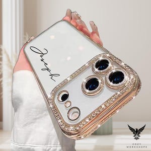 May include: A clear phone case with a gold-colored frame and sparkling rhinestones. The case has a white backing with the name "Joseph" in black script. The camera lenses are surrounded by gold and rhinestones. The Cozy Workshops logo is in the bottom right corner.