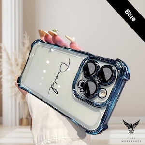 May include: A clear phone case with a blue bumper. The case has the name "David" in cursive script. The phone case has a black bar that says "Blue". The case has a logo that says "Cozy Workshops".
