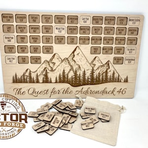 May include: A wooden board with a mountain scene and the text "The Quest for the Adirondack 46". There are 46 small wooden squares with the names of mountains on them. The squares are in a burlap bag.