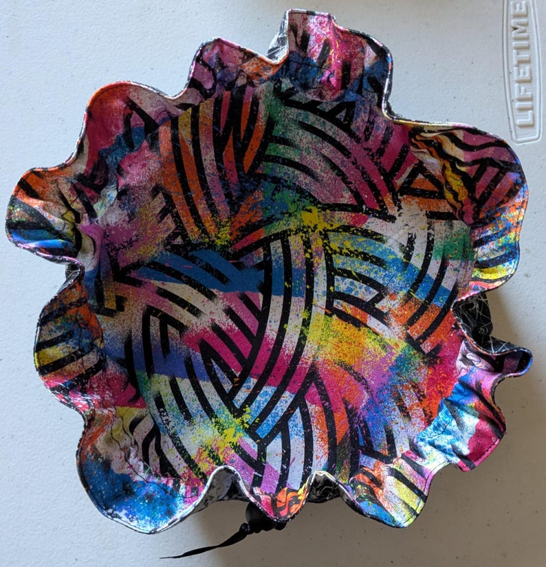 May include: A colorful, abstract bowl with a scalloped edge. The bowl features a vibrant design of black curved lines and multicolored paint splatters in shades of pink, blue, yellow, and orange. The bowl is approximately 10 inches in diameter.