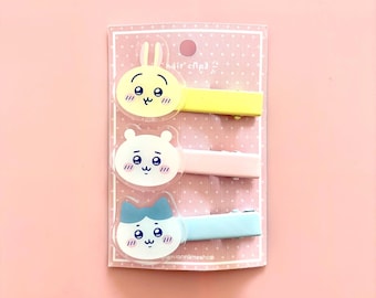 May include: A set of three hair clips attached to a pink polka-dot card labeled hair clips. The clips feature cartoon animal faces: a yellow rabbit, a white bear, and a light blue cat, each with blushing cheeks and a simple facial expression.