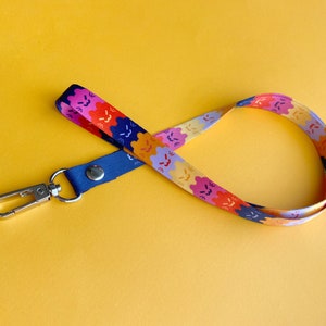 May include: A colorful lanyard with a silver clip. The lanyard has a repeating pattern of smiling faces in various colors, including pink, orange, yellow, and blue.