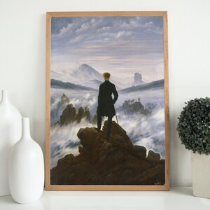 May include: A painting depicting a lone figure standing on a rocky outcrop overlooking a sea of clouds. The figure is wearing a dark coat and hat, and is holding a walking stick. The sky is a pale blue, and the clouds are white and fluffy.