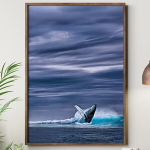May include: A framed print depicts a whale breaching the ocean's surface. The artwork features a dark blue sky with dramatic cloud formations. The whale's tail is visible above a turquoise wave, creating a dynamic ocean scene.