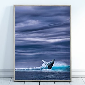 May include: Framed art print depicting a breaching whale in a turquoise wave. The whale's dark body contrasts with the white spray and the deep blue ocean. The sky is filled with dark, dramatic clouds, creating a moody seascape.