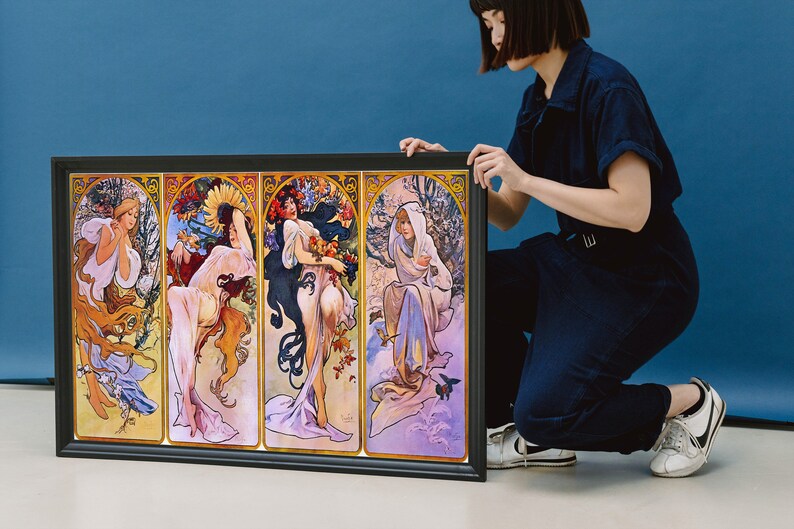 May include: A framed print depicting four women representing the four seasons. Each woman is shown in a different colour scheme and surrounded by flowers and foliage. The print is in a black frame and is being held by a person.