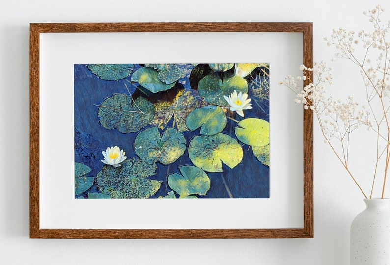 Op de afbeelding: Een ingelijste foto van witte waterlelies met groene bladeren die op een blauwe vijver drijven.