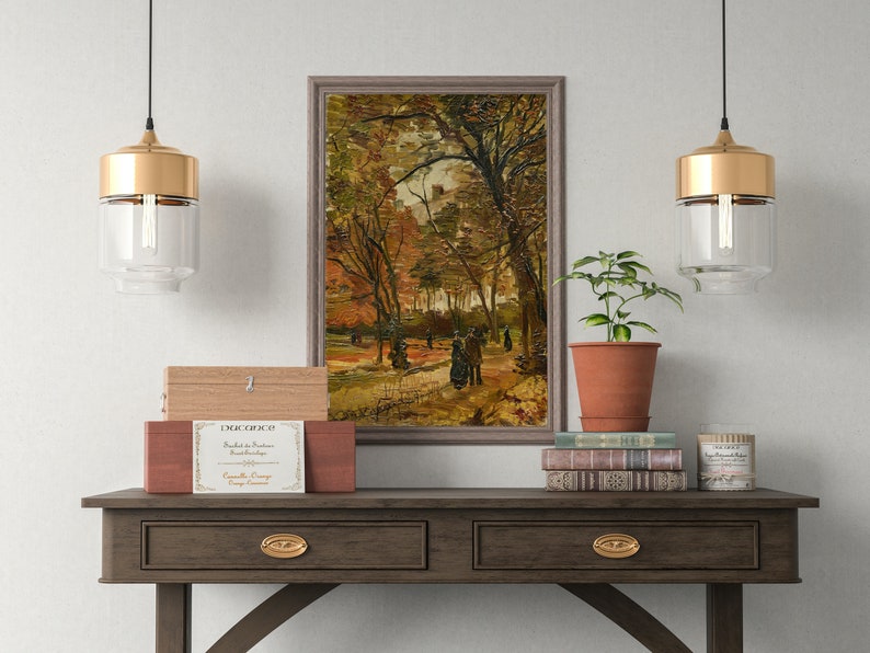 K&ouml;nnte beinhalten: Ein gerahmtes Gem&auml;lde, das eine Waldszene mit Personen zeigt, die auf einem Weg gehen. Das Gem&auml;lde h&auml;ngt an einer Wand &uuml;ber einem Holz-Konsolentisch mit zwei Schubladen. Zwei goldene Pendelleuchten h&auml;ngen &uuml;ber dem Tisch, und eine Topfpflanze und B&uuml;cher stehen auf dem Tisch.