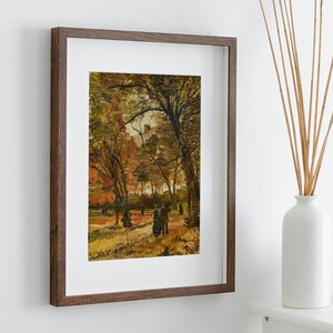 K&ouml;nnte beinhalten: Ein gerahmtes Gem&auml;lde, das eine Herbstlandschaft mit Menschen zeigt, die durch einen Park gehen. Das Gem&auml;lde ist in einem braunen Holzrahmen.