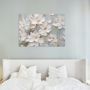 The tranquil bedroom features a white flower painting above a bed with white linens against a light blue wall