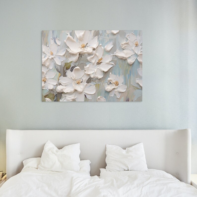 The tranquil bedroom features a white flower painting above a bed with white linens against a light blue wall