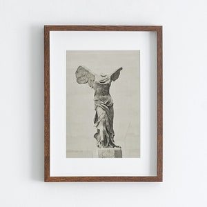 May include: A framed black and white photograph of the Winged Victory of Samothrace statue. The statue is headless and has its arms outstretched. The statue is on a pedestal.
