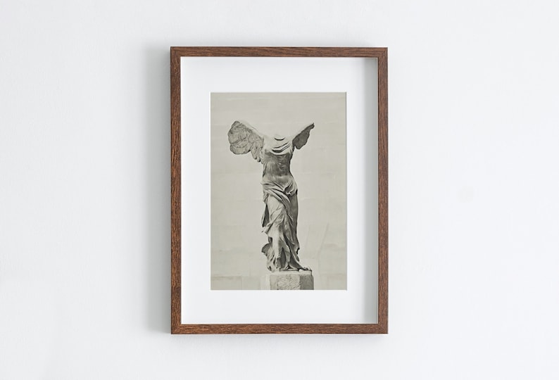 May include: A framed black and white photograph of the Winged Victory of Samothrace statue. The statue is headless and has its arms outstretched. The statue is on a pedestal.