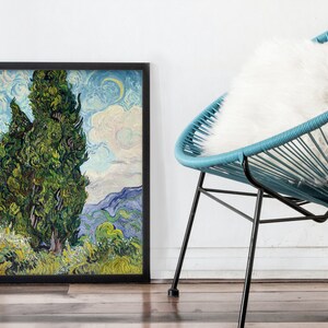 May include: A framed painting of two tall, green cypress trees against a blue and white sky with a crescent moon. The painting is in a black frame and is hanging on a white wall.